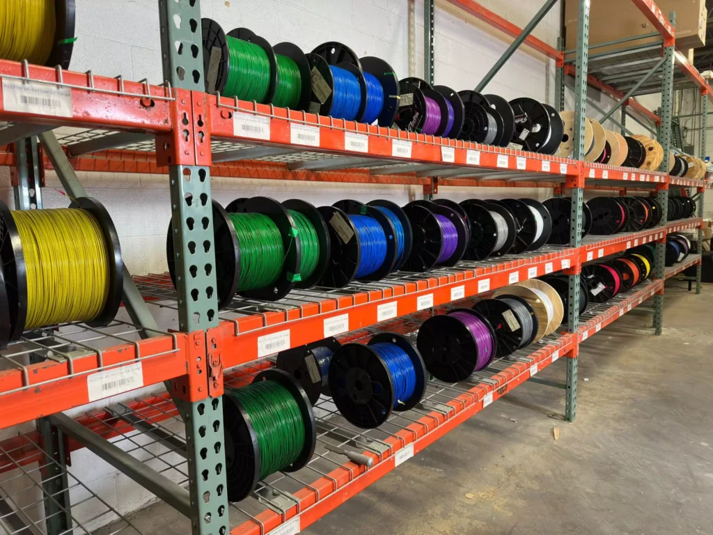 Spools of M22759/16 wire on shelves, showcasing various colors for car wiring and military specifications